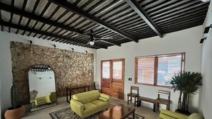 A spacious living room with a stone wall, a ceiling fan, and a large window with blinds. - Charming 2-bedroom house with AC, WiFi in superb Mérida (Mérida)