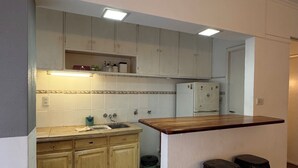 A kitchen with wooden cabinets, a sink, and a bar area with stools. - Rincón del Edén ~ Apartment in front of the casino and 1 block from the sea ☀️ (Mar del Plata)