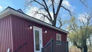 A red building with a white door, a small porch, and a stone wall in front. - Broken Willow Bungalow (Eau Claire)