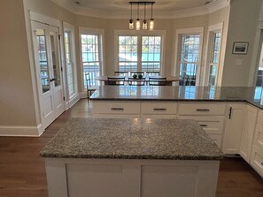 Una cocina con encimera de granito, armarios blancos y un comedor con mesa y sillas.