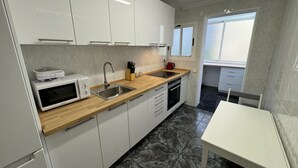 Une cuisine moderne avec des meubles blancs, un four à micro-ondes, un évier et un plan de travail en bois.