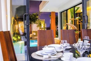 A dining area with a table set for two, a glass partition, and a view of an outdoor pool area.