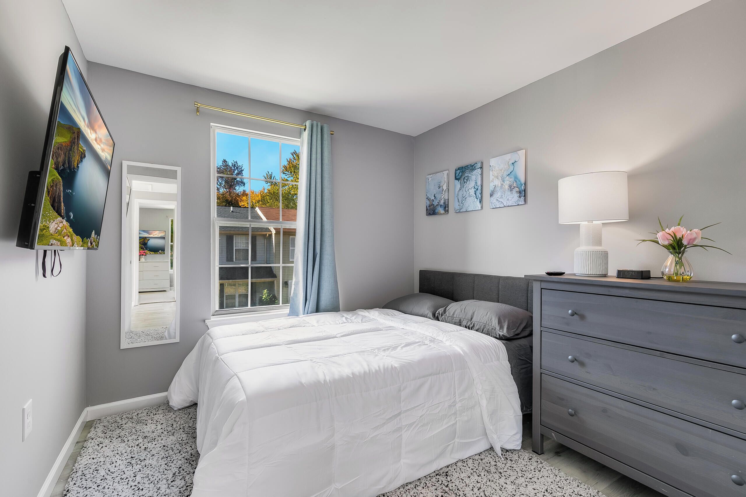 A bedroom with a large bed, a dresser, a TV, and artwork on the wall.