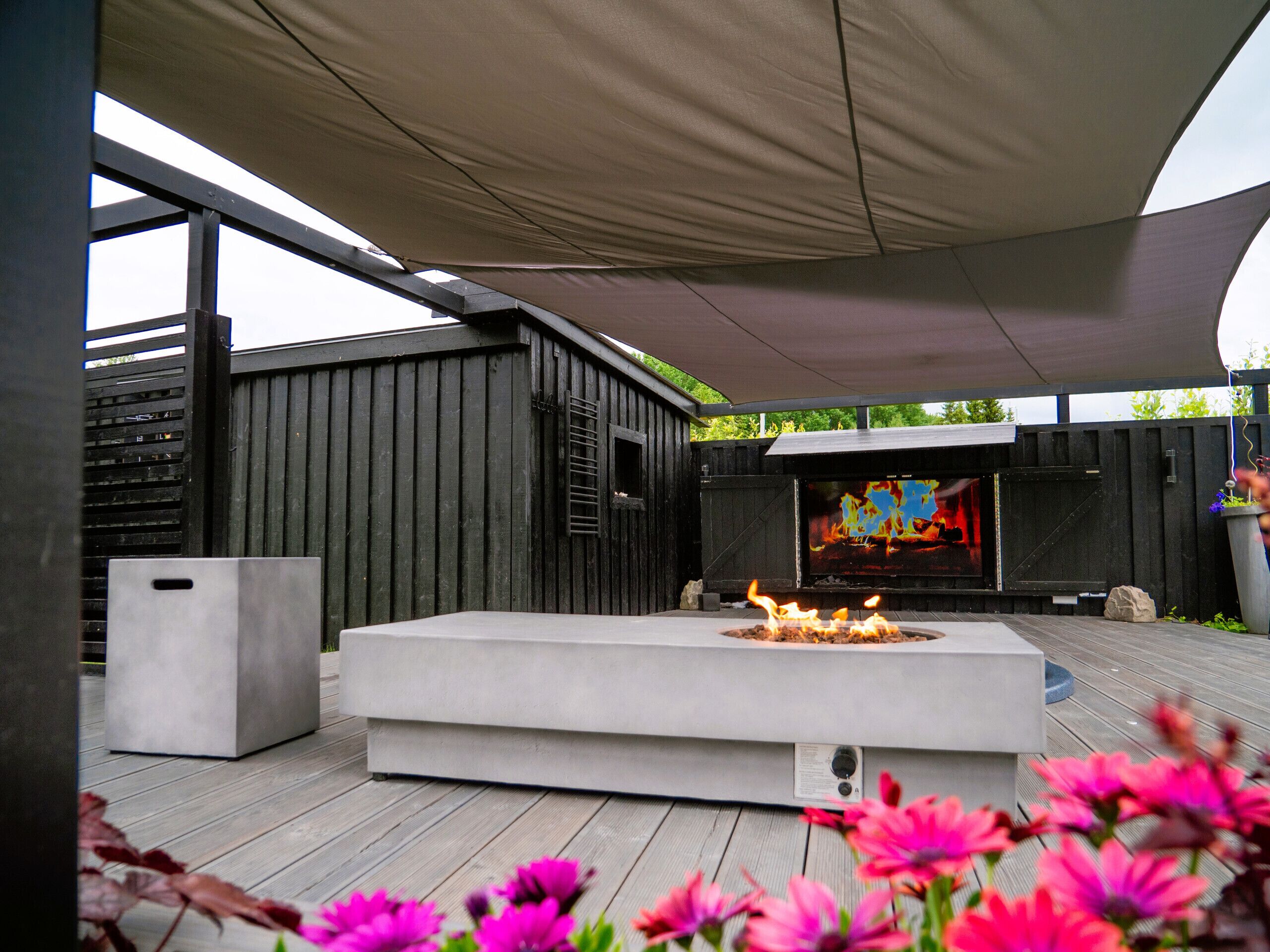 Un patio extérieur moderne doté d’un foyer, d’un écran de télévision et d’une terrasse en bois.