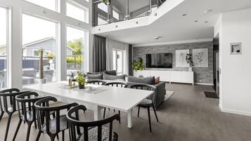 Een ruime woonkamer met een eettafel, stoelen en een bank. Er is een balkon met een hekwerk en potplanten.