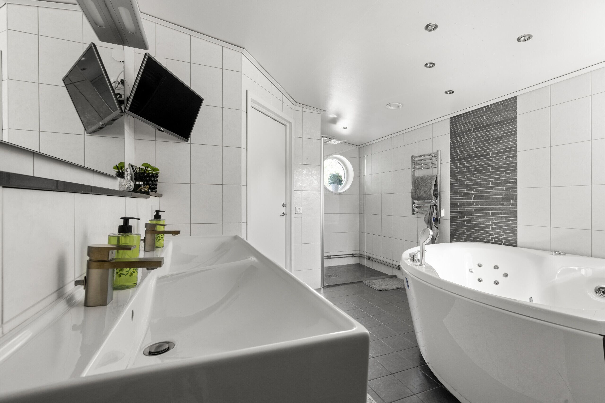 Une salle de bain moderne avec une grande baignoire blanche, un lavabo doté de distributeurs de savon verts et un miroir au-dessus du lavabo.
