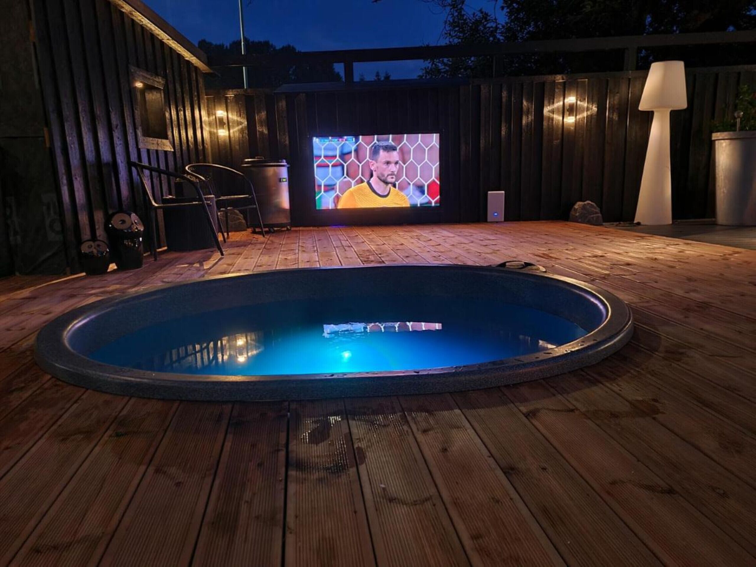 Un bain à remous doté d’une terrasse en bois et d’un écran de télévision diffusant un événement sportif.