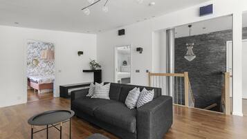 Een moderne woonkamer met een grijze bank, een klein rond tafeltje en een trap naar een verdieping boven.