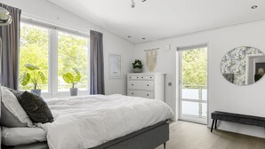Ein modernes Schlafzimmer mit einem großen Bett, einem Schminktisch, einer Bank und Blick ins Grüne.