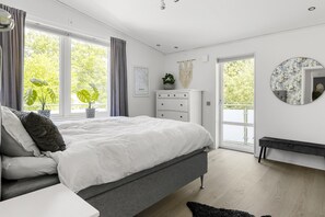 Une chambre à coucher moderne avec un grand lit, une commode, un banc et une vue sur la verdure.