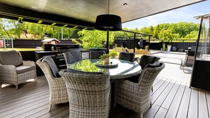 Eine Terrasse im Freien mit Korbmöbeln, einem runden Tisch und einer hängenden Lampe.