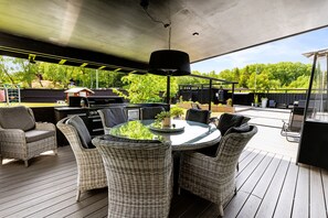 Une terrasse extérieure avec des meubles en osier, une table ronde et un luminaire suspendu.