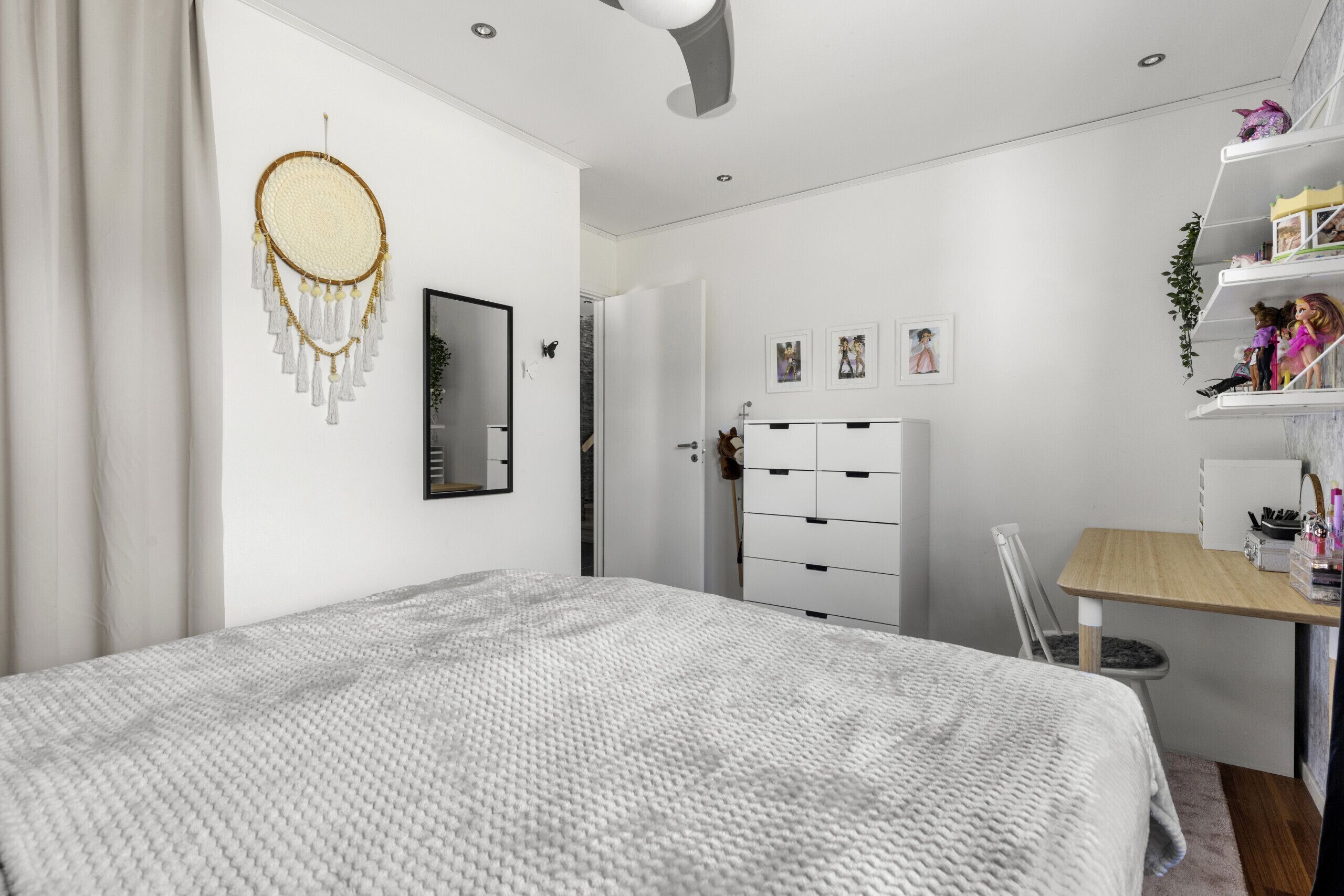 Une chambre moderne avec un grand lit, un bureau avec une chaise, une armoire et un attrape-rêves accroché au mur.
