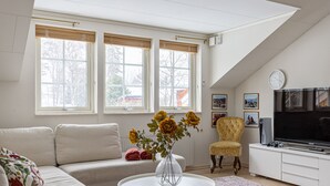 Ein Wohnzimmer mit einer Couch, einem runden Couchtisch mit Blumen in einer Vase, einem Fernseher und einem Sessel.