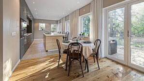 A modern kitchen with a central island, a dining area with a round table and chairs, and large sliding glass doors leading to a backyard. - Modern villa with Jacuzzi (Vega)