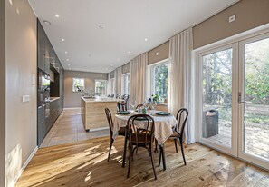 Una cocina moderna con una isla central, un comedor con una mesa redonda y sillas, y grandes puertas correderas de vidrio que dan a un jardín trasero.