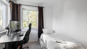 A bedroom with a single bed, a desk with a computer, and a window with curtains.