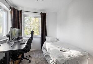 A bedroom with a single bed, a desk with a computer, and a window with curtains.