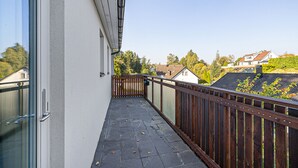 A balcony with a wooden railing, a glass door, and a view of houses and trees in the background. - Modern villa with Jacuzzi (Vega)