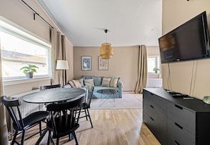 Una sala moderna con comedor, un conjunto de sofás, un televisor y un amplio ventanal con cortinas.