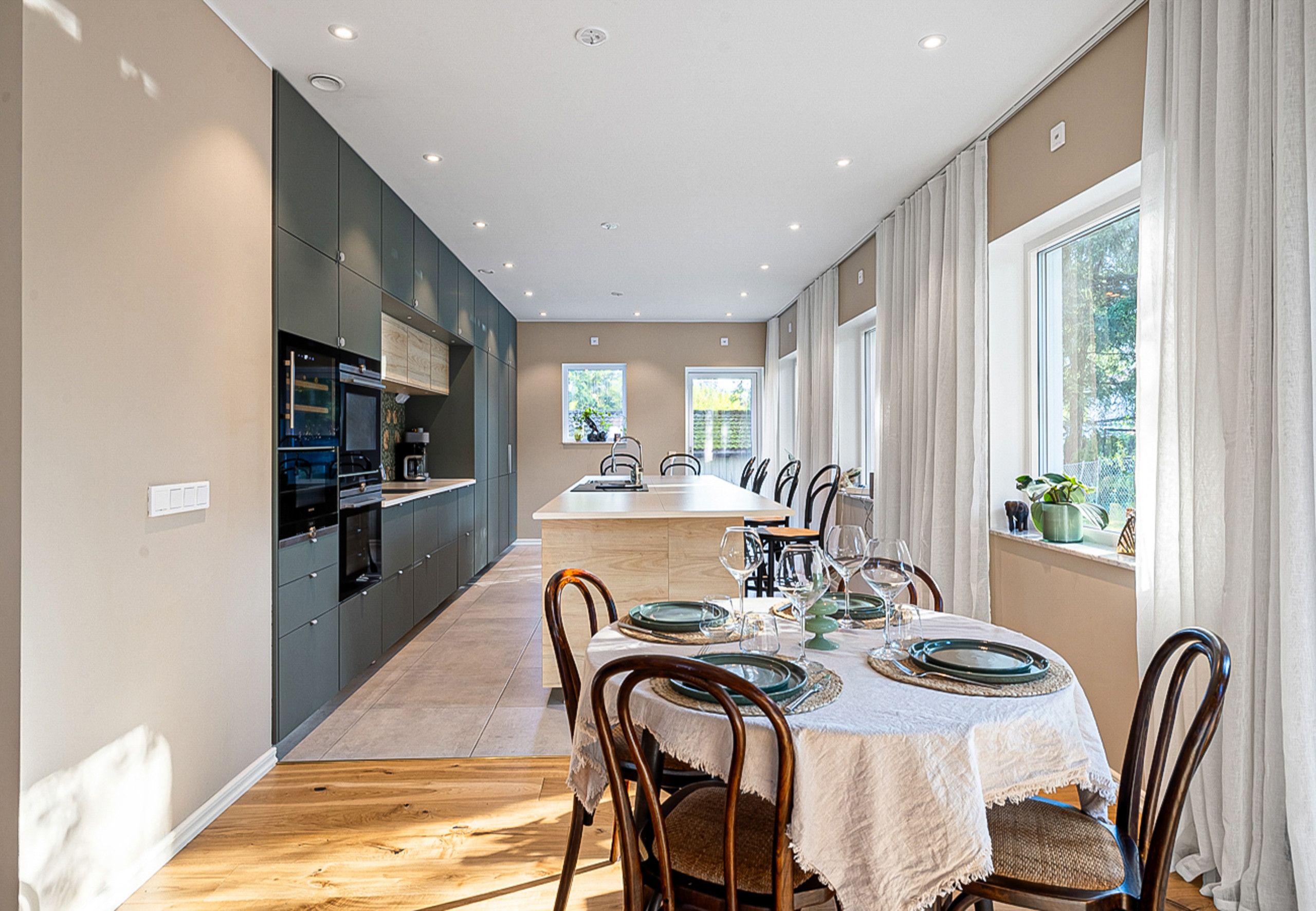 A modern kitchen with dark cabinets, a central island, and a dining area with a white tablecloth and wooden chairs.