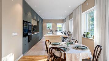 A modern kitchen with dark cabinets, a central island, and a dining area with a white tablecloth and wooden chairs.