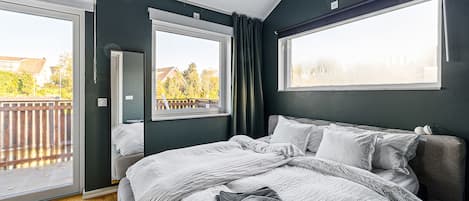 A bedroom with a large bed, a sliding glass door to a balcony, and a view of the outside.