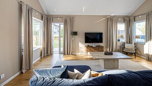 Ein geräumiges Wohnzimmer mit einem großen Flachbildfernseher, einer Couch, einem Couchtisch und einem Sessel.