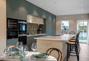 A modern kitchen with built-in appliances, a dining area with chairs, and a view of the outdoors.