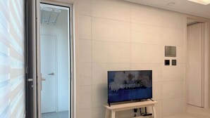 Ein modernes Zimmer mit Fernseher auf einem Standfuß, einer Schiebetür und einer hell gefliesten Wand.