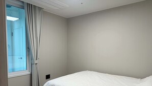 Ein Schlafzimmer mit einem Einzelbett, einem Fenster mit Vorhängen und einem Lichtschalter an der Wand.