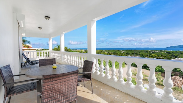 A covered outdoor seating area with a table and chairs, a view of the landscape, and a white balustrade. - Spacious 3-bedroom, 2-bathroom apartment with AC in The Valley (The Valley)