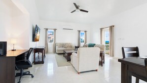 A spacious living area with a sofa, armchairs, a coffee table, and a TV. There is a ceiling fan, a window with curtains, and a view of the outdoors. - Spacious 3-bedroom, 2-bathroom apartment with AC in The Valley (The Valley)