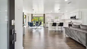 A modern kitchen with white cabinets, a central island with bar stools, and a dining area with blue chairs. - Modern 3bed, 2bath House in Wesley Chapel, with EV Charging Outlet, AC, & WiFi.  (Zephyrhills)