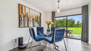 A modern room with a large painting, blue chairs, a table, and a view of a green landscape through large windows. - Modern 3bed, 2bath House in Wesley Chapel, with EV Charging Outlet, AC, & WiFi.  (Zephyrhills)