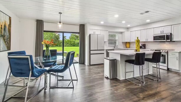 A modern kitchen with white cabinets, a central island, and a dining area with blue chairs. - Modern 3bed, 2bath House in Wesley Chapel, with EV Charging Outlet, AC, & WiFi.  (Zephyrhills)