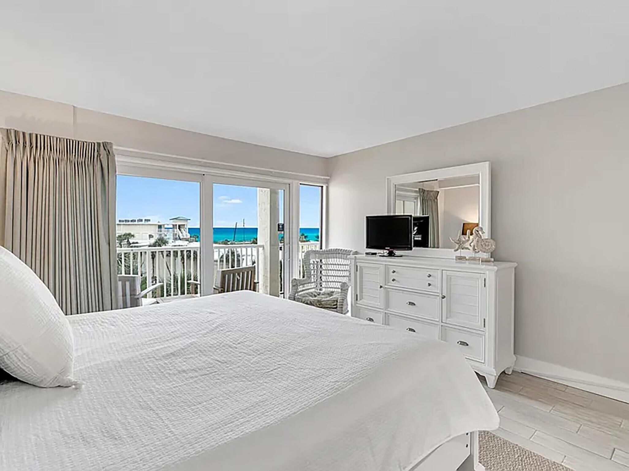 A bedroom with a bed, a dresser, a TV, and a balcony with a view of the ocean.