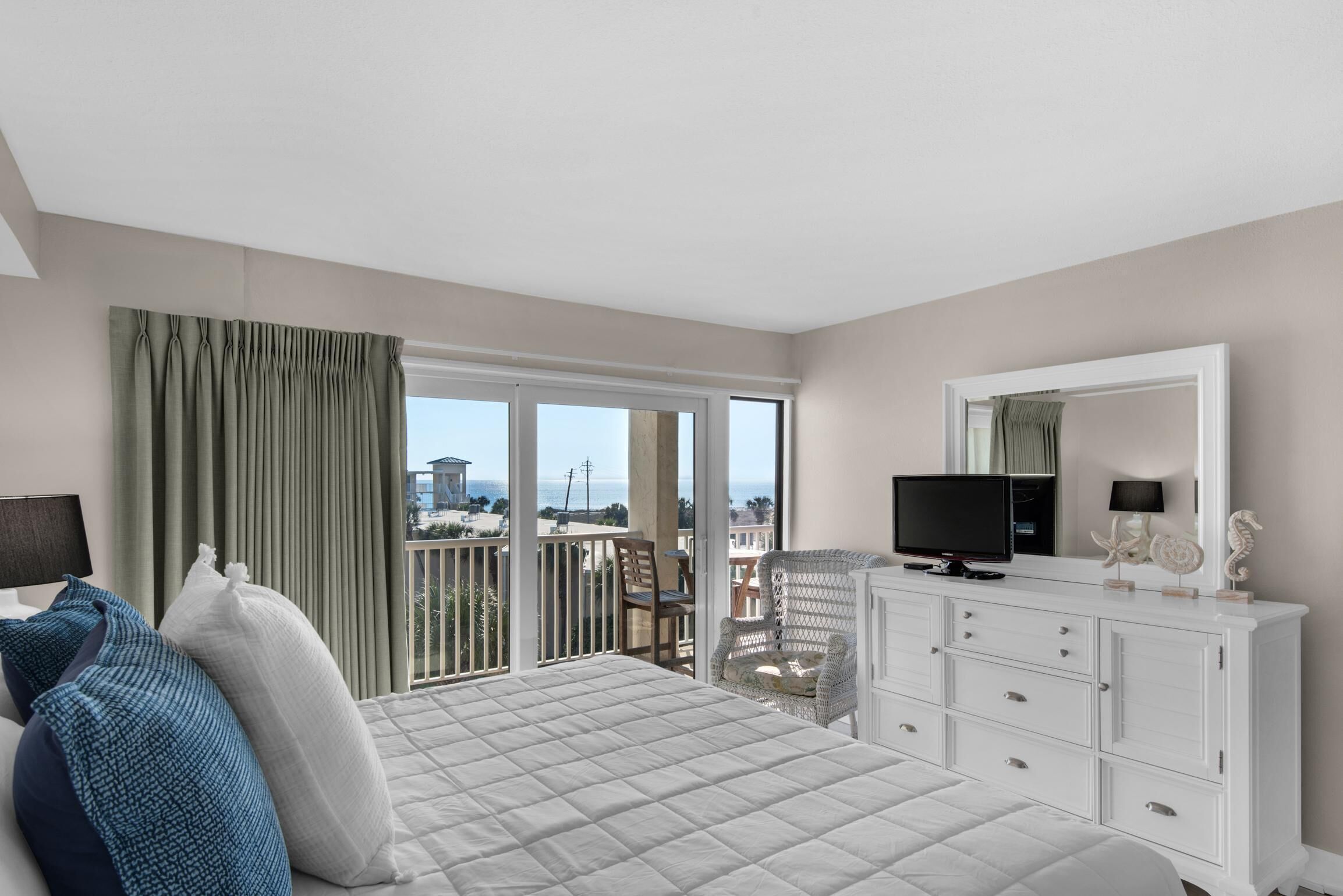 A hotel room with a bed, a TV, a dresser, and a balcony with a view of the sea.