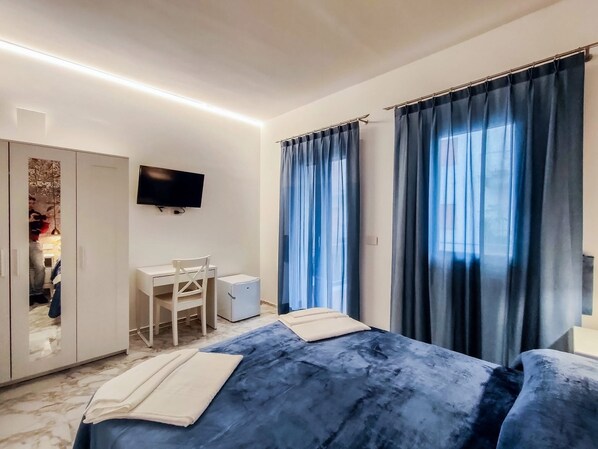 Habitación de hotel con cama, escritorio, silla, televisor y armario.