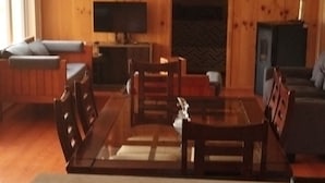 Een kamer met houten lambrisering, een eettafel, stoelen, een bank en een televisie.