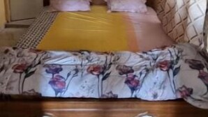 Een slaapkamer met een bed, een houten hoofdbord, een gele deken en een bloemenbed overtrek.