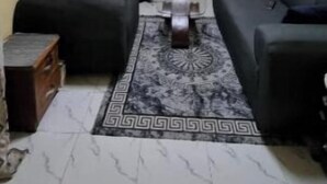 Een woonkamer met twee zwarte banken, een salontafel, een televisie op een standaard, behang met een patroon en een vloer met een marmerprint.
