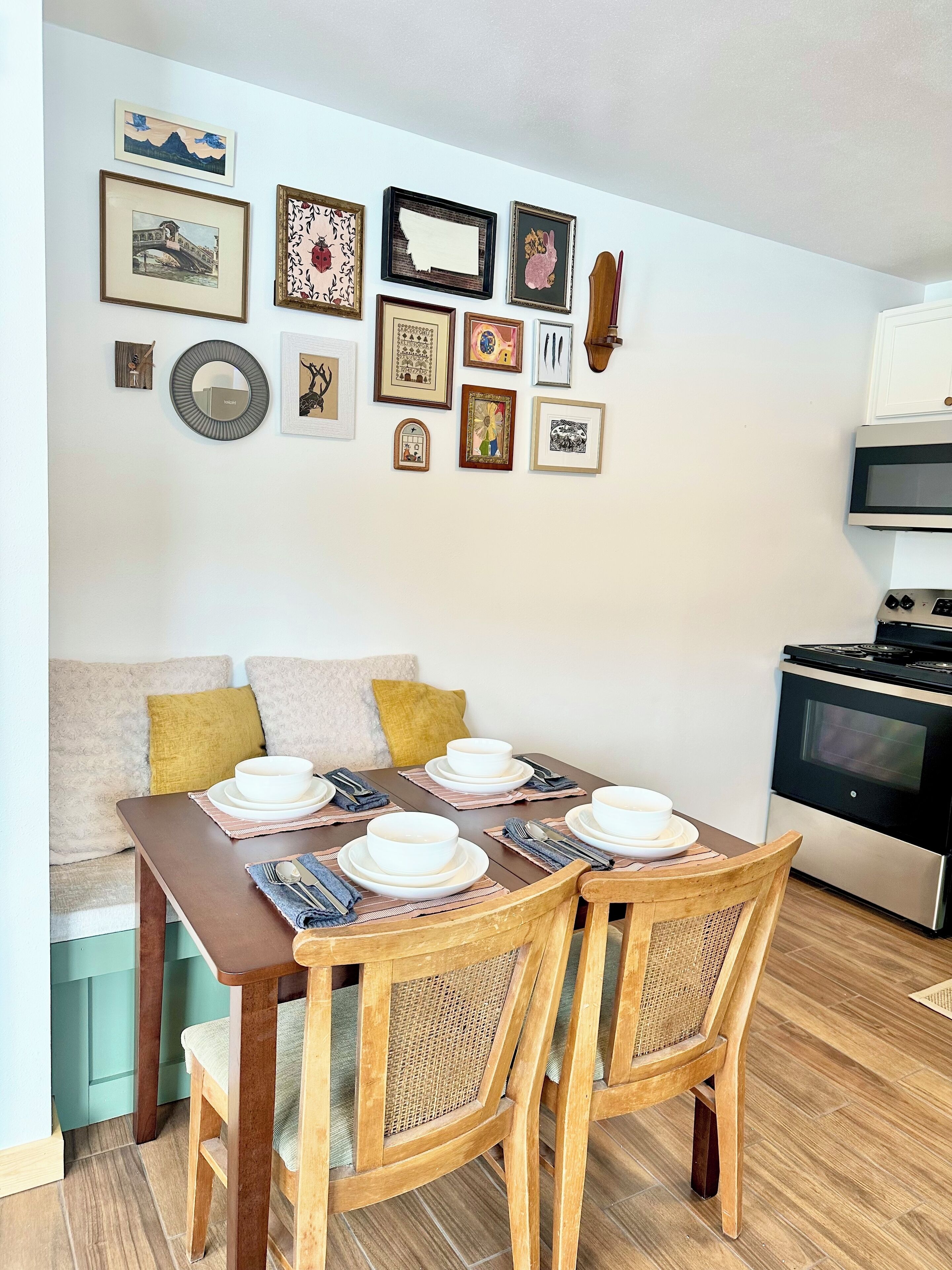 A dining area with a wooden table set for four, a sofa with cushions, and a kitchen with a stove and microwave.