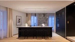 A modern kitchen with a central island, bar stools, a marble backsplash, and pendant lighting. - Les Suites by Cave Vauban - Suite Caria (Dijon)