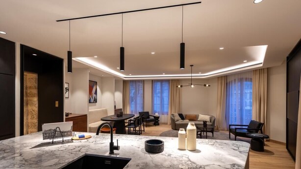 A modern kitchen with a marble countertop, black sink, and pendant lighting. - Les Suites by Cave Vauban - Suite Caria (Dijon)
