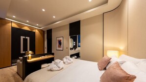 A modern hotel room with a large bed, a desk, a mirror, and a bathroom. - Les Suites by Cave Vauban - Suite Caria (Dijon)