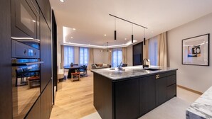 A modern kitchen with a large island, dark cabinetry, and pendant lighting. - Les Suites by Cave Vauban - Suite Caria (Dijon)