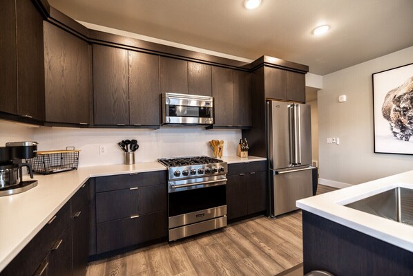 A modern kitchen with dark wood cabinets, stainless steel appliances, and a wooden floor.