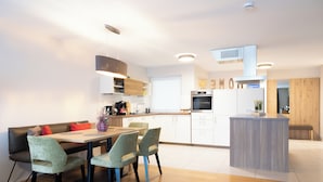 Ett modernt kök med matplats, utrustat med en central köksö, inbyggda vitvaror och en träbänk.