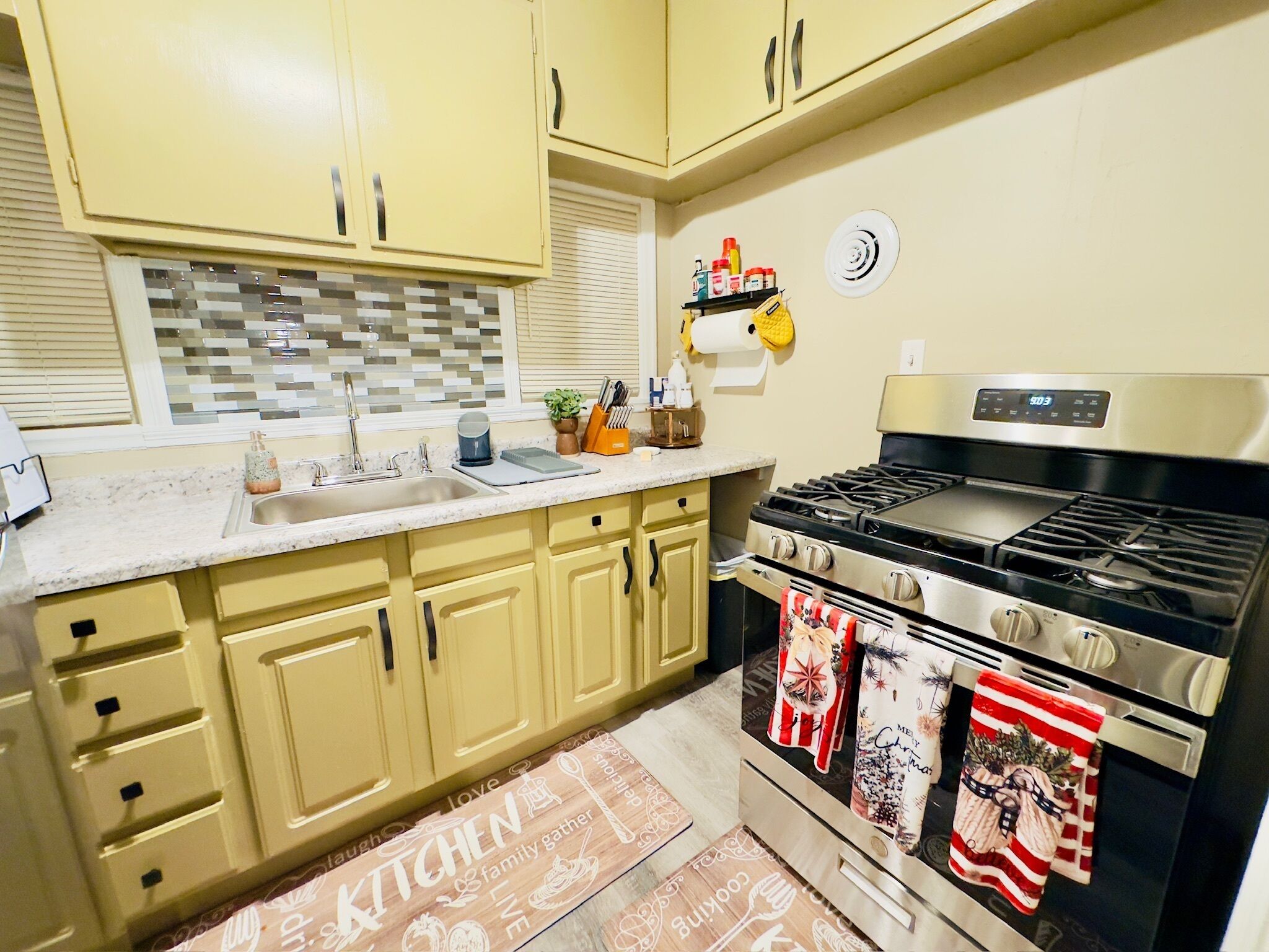 Una cocina con armarios amarillos, estufa de acero inoxidable y salpicadero de azulejos.